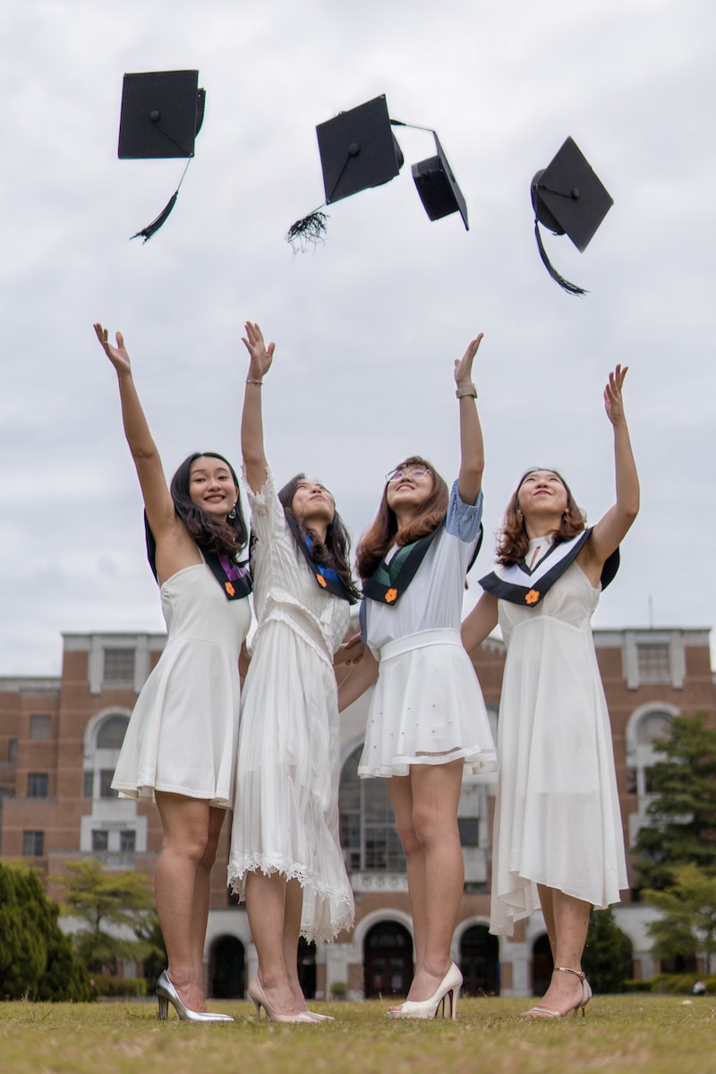 low-angle photography of four girls throwing mortar hat near outdoor during daytime